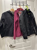Three women's jackets (black Burton, dark pink fleece, black padded) hanging on door hooks