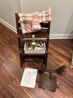 Full view of high chair with cushion, harness, plastic bracket and manual in front