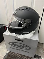 Matte black adult medium HJC motorcycle helmet sitting on top of its original box showing side and front with clear visor down.