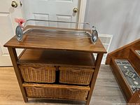 Wooden cabinet with three woven wicker baskets visible and metal towel rack placed on top.