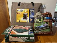 Photo of camping gear on table showing Coleman Quickbed mattress box, Ozark Trail twin mattress box, and Broadstone portable closet in carry bag