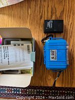 Blue hard case closed next to Canon NB-6L battery, battery charger, and user manual on wooden table