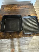 Top-down view of the square cast iron pan and ribbed grill pan lid on a wooden table.