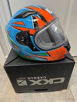 Side view of the fully assembled child's CKX helmet with bright blue, orange, green, and white graphics on black stand box.