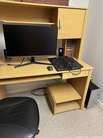 Photo of Samsung monitor, two keyboards, wired mouse, and speaker on a light wood desk with chair