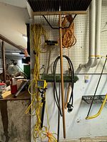 Photo showing barn broom, extension cords, halogen work light, bow saw, and wire scrubber hanging on pegboard wall.