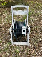 Front view of a black garden hose neatly coiled on a white plastic hose reel with a handle for winding.