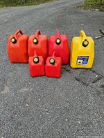 Seven gas cans including six red fuel containers and one yellow diesel can, all with caps, placed on outdoor pavement.