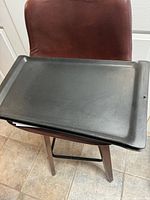Top-down photo of rectangular black cast iron griddle placed on a brown chair showing flat surface and raised edges.
