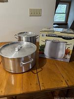 Two large aluminum stockpots with lids on wooden table beside box showing Hendricks Stockpot Marmite branding