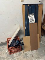 Unassembled workbench parts stacked against wall including metal frame pieces, wooden panels, and plastic crate with smaller parts.
