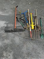 Photo of a group of garden tools including rakes, propane weeder, shovels, pitchfork, and cultivator.