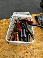 Basket with various hand tools including pliers, wrenches, and screwdrivers on a wooden surface.