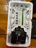 Small white quadcopter drone and black remote control in white foam packaging