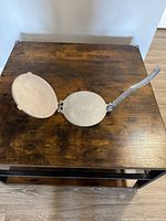 Top view of the open metal tortilla maker showing the inside pressing surfaces and the long handle.