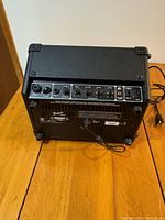 Rear view showing control panel with two channel inputs, knobs for volume, bass, treble, tone and power switch, power cord and charger connection port