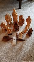 Photo showing all 11 wood statues and 1 wooden spoon arranged on carpet floor.