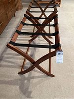 Angle showing two folding luggage racks standing side by side with black nylon straps and brown wood cross legs.