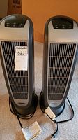 Front view of two Lasko tower heaters side by side showing full units and power cords
