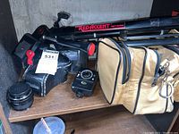 Canon camera body and lenses placed on wooden shelf alongside light meter, tripod, and camera bag.