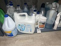 Photo showing assorted cleaning supply containers including jugs and spray bottles, many labeled Bona Hardwood Floor Cleaner in a basement utility room.