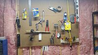 Pegboard with various hand tools hanging including a wire stripper, locking pliers, wrench, clamp, and hack saw