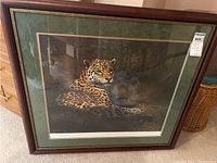 Framed artwork featuring a jaguar lying down, with green mat and wooden frame, photo taken to show front view.