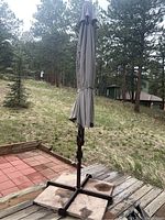 Overall view of the closed large patio umbrella with stand set on a wooden and tile deck outdoors.
