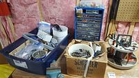 Overview of hardware items in blue tote, cardboard boxes, nuts and bolts organizer, and vise in basement work area