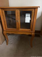 Night stand front view showing light brown wood finish, curved legs, and two glass doors with brass knobs