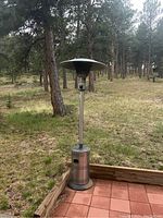 Full view of the Blue Rhino outdoor patio heater placed on a tiled patio section with grassy wooded area in the background