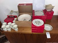 Photo showing the entire set of dinnerware including plates, bowls, mugs, and serving bowls mostly in boxes on a wooden surface.