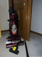 Red Shark upright vacuum cleaner with cord wrapped around, dust container visible, placed indoors on carpet