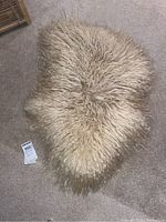 Full view of small, irregular-shaped fluffy sheep wool rug lying on carpet floor.