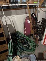 Wheelbarrow with scratches and multiple garden hoses coiled next to it