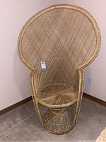 Full view of the large wicker peacock chair against a plain wall on carpeted floor showing the high rounded back and woven details.