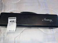 Closed black hard case with 'Armstrong' logo embossed on top and auction tag attached.