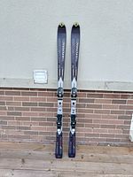 Full view of both skis resting upright against a brick wall showing length and bindings.