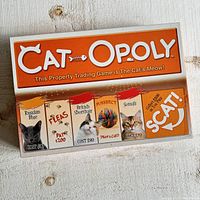 Photo of game box front showing Catopoly title and samples of game cards featuring cat breeds and themed property names.