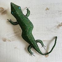 Top view of the green beaded gecko lizard metal wall hanging showing full body and blue bead eyes on a wood surface.