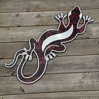 Full view of the large gecko-shaped wall hanging with mosaic red tiles and mirror accents on a wooden surface.