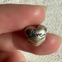 Close up of front face of heart charm showing engraved 'love' script.