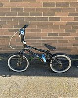 Side view of the left side of the black children's bike against brick wall, showing frame and tires.