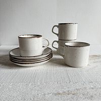Set of four stacked mugs with matching saucers, showing cylindrical mug shape and brown speckled design with rims.