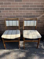 Set of two mid century wood chairs with fabric backs and seats, showing front view against brick background
