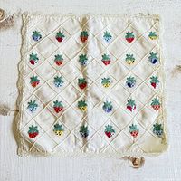 Full view of one pillow cover showing embroidered strawberries in multiple colors arranged in a diamond grid pattern on off-white fabric with lace trim