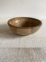 Side view of small pottery bowl showing speckled glaze with brown and cream tones