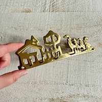 Front view of brass key organizer held in hand showing house, tree, and geese design with three hooks.