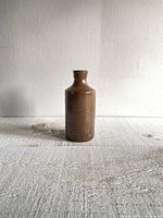 Front view of brown vitreous stoneware bottle with embossed markings showing producer and origin.