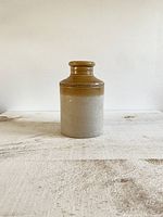Full front view of vintage two tone pottery crock vessel showing brown top with bead detail and beige lower body with stamped mark near base.